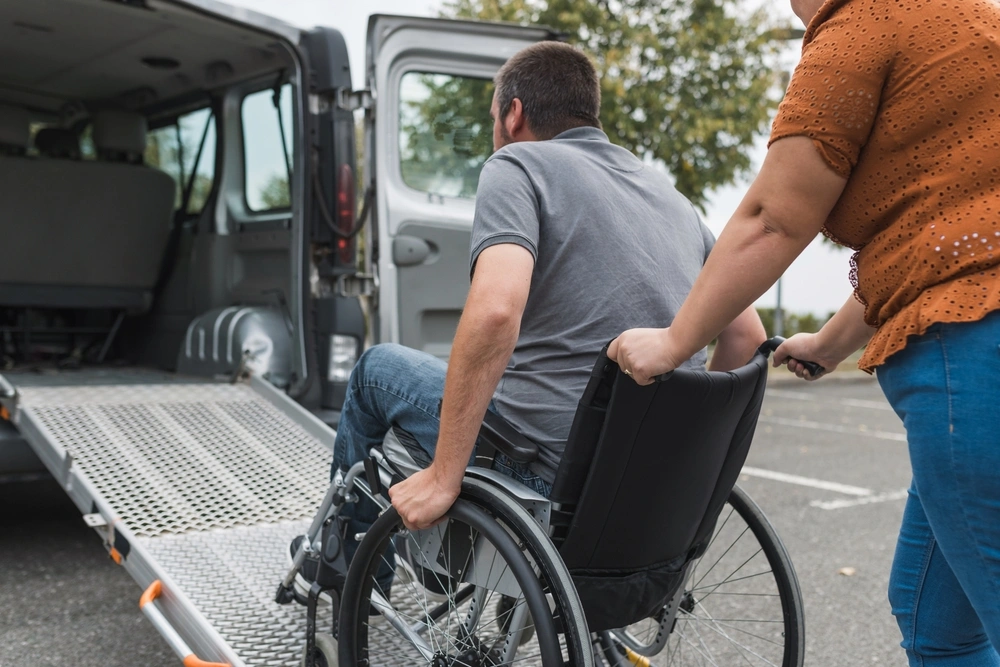 carer helping disabled men on wheelchair get in a van
